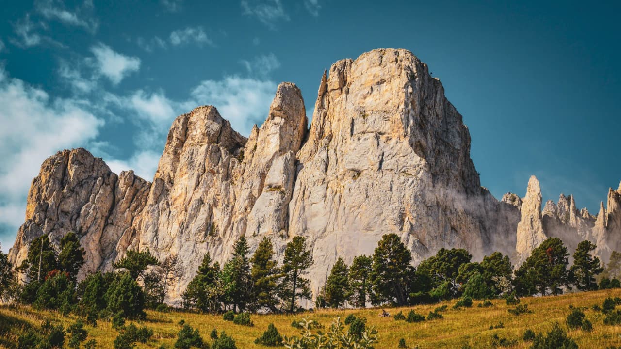 Majestic cliffs rising above lush green meadows under a clear blue sky, inviting adventure.