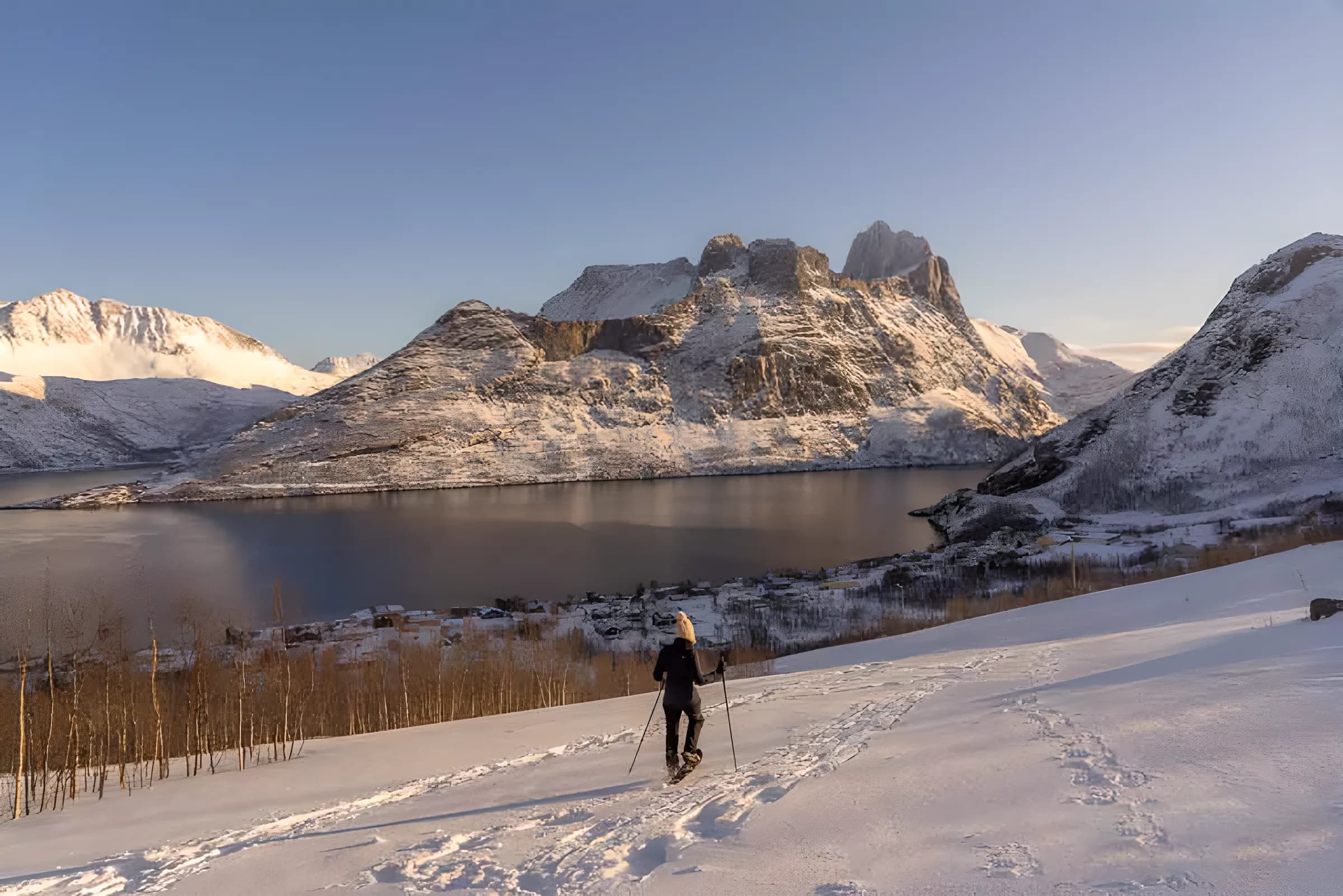 A man on snowshoes on a snow-covered mountain, with a panoramic view of the fjords and peaks of Norway.