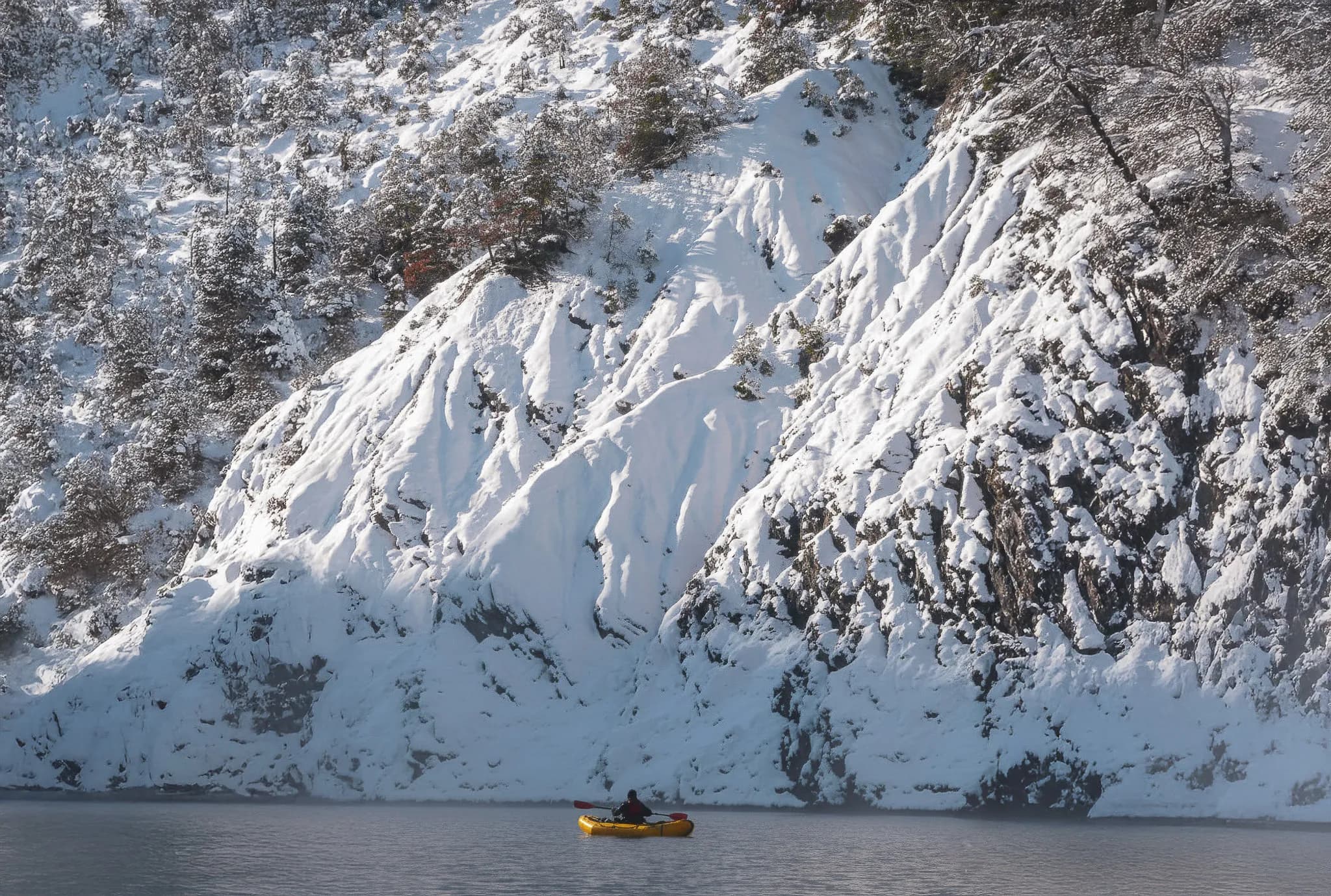 Un aventurier en packraft sur le lac de Serre-Ponçon, entouré d'une nature hivernale époustouflante.