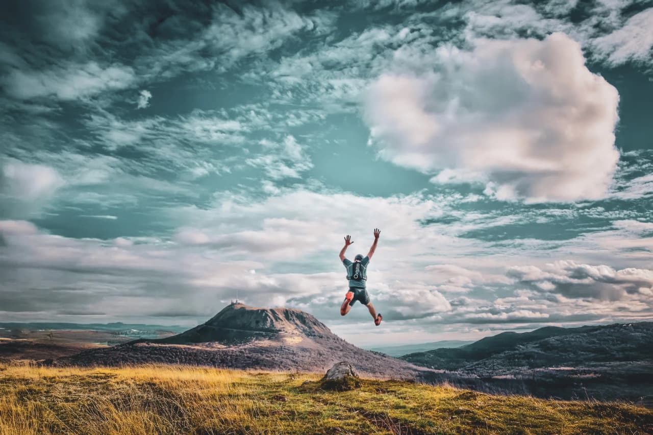 A wilderness athlete leaps energetically down a volcanic path under a magnificent sky.