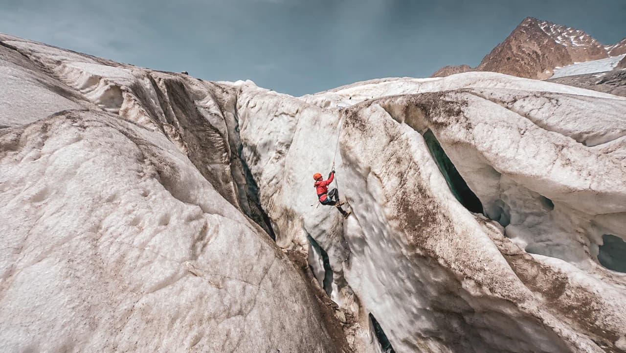 Un alpiniste grimpe sur un glacier majestueux dans les Écrins, sous un ciel impressionnant.