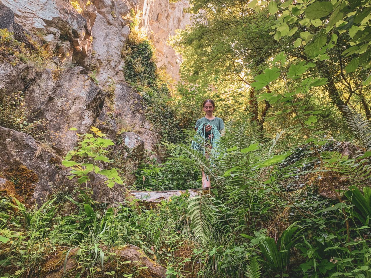 A smiling climber stands among lush greenery and rocky outcrops in Belgium.