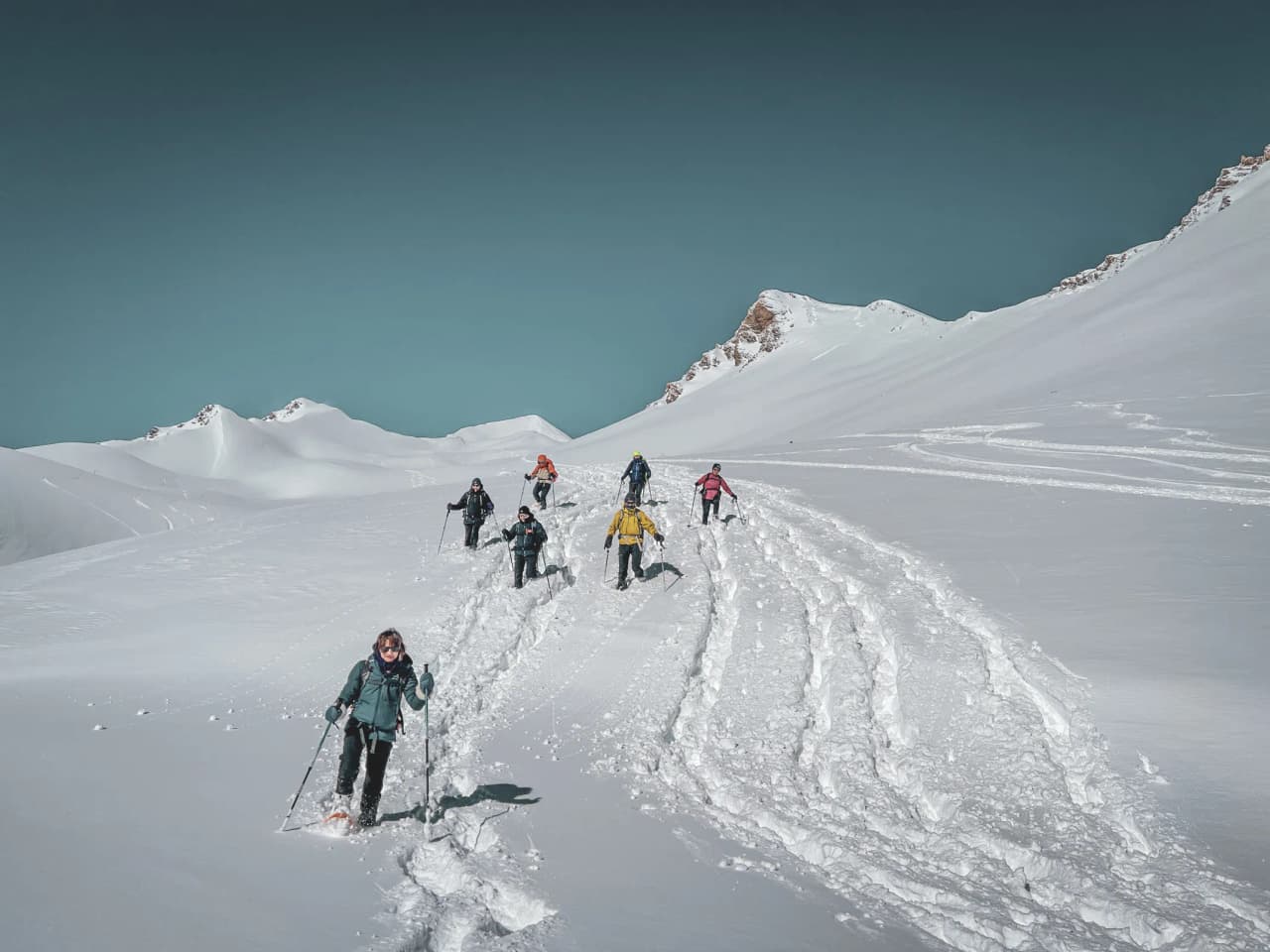 Groupe de randonneurs en raquettes, cheminant sur un plateau enneigé face aux majestueux glaciers.