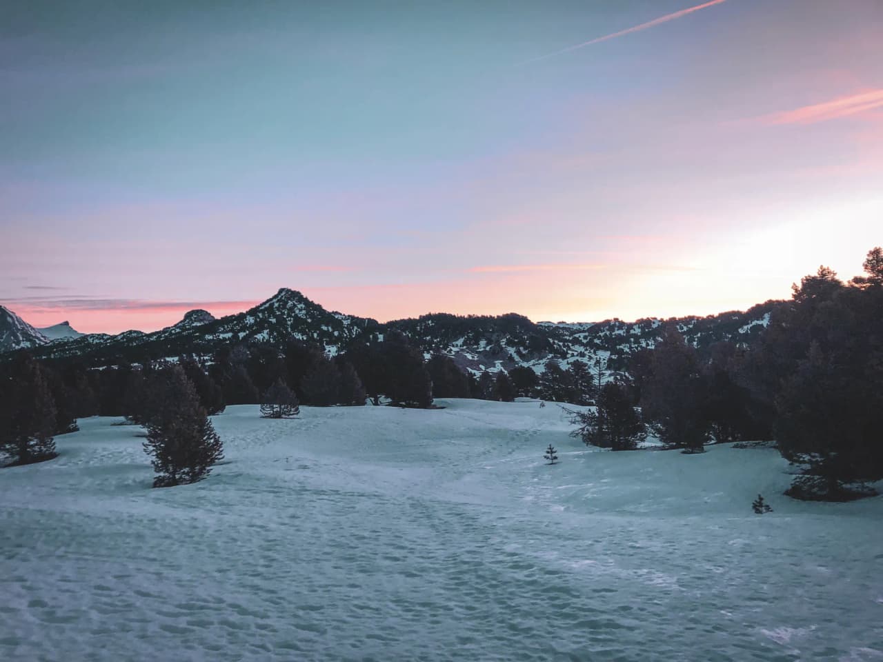 A snowy landscape with mountains under a pastel sky, a promise of snowshoeing adventures.