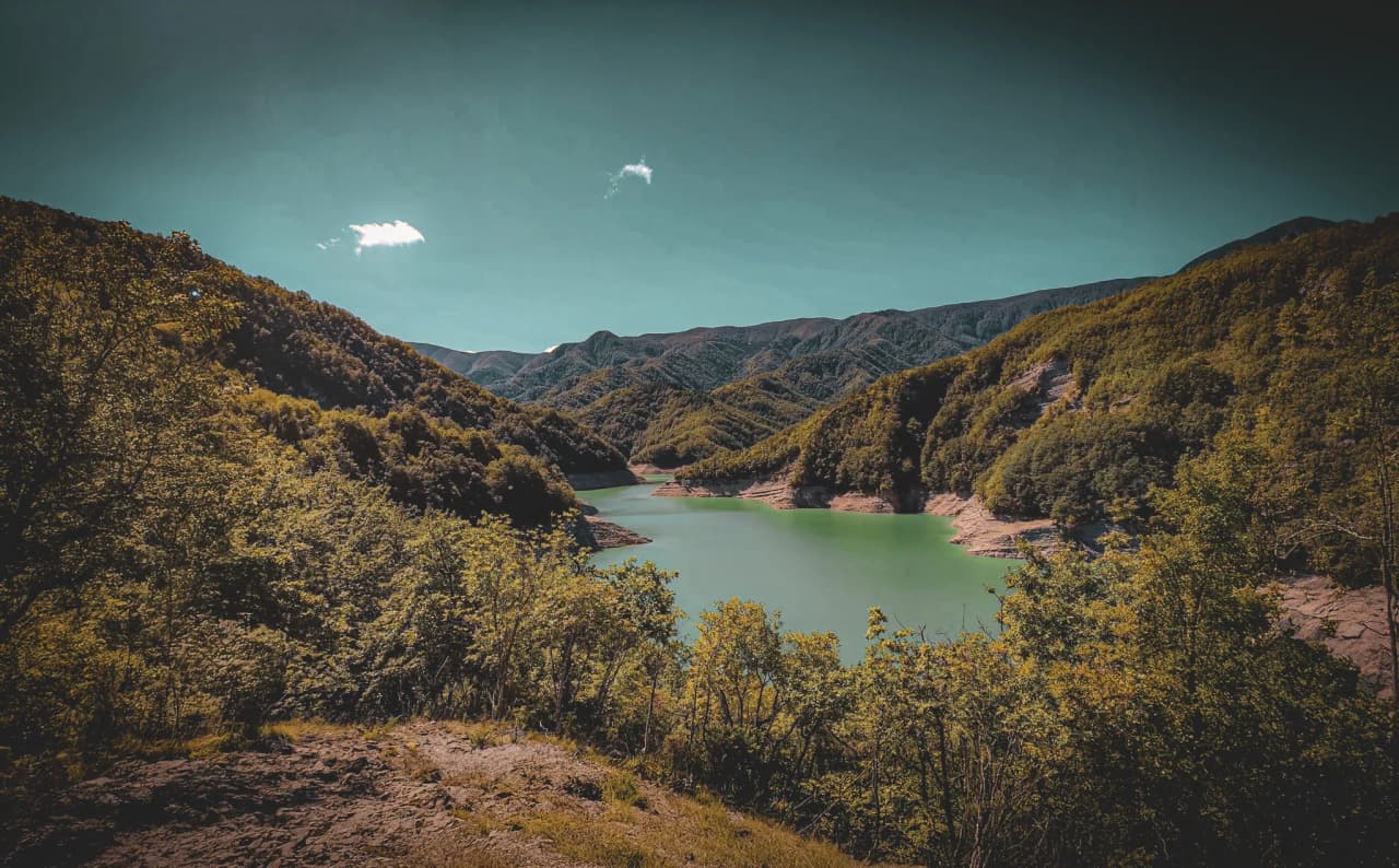 Lago Ridracoli, in Tuscany, Italy. A natural landscape with a lake of green waters surrounded by green hills and mountains. The sky is clear, with a few floating white clouds.