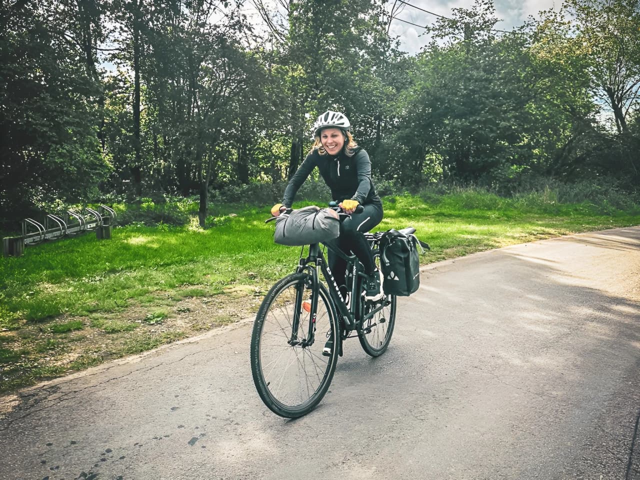 Femme souriante à vélo sur un chemin verdoyant, prêt pour l'aventure dans les Hautes Fagnes.