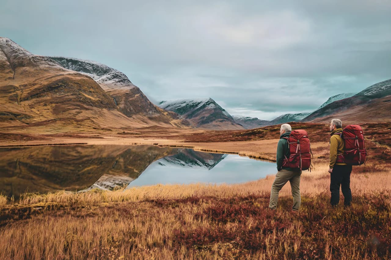 Two hikers contemplate a mirror-like mountain landscape in a wild and peaceful environment.
