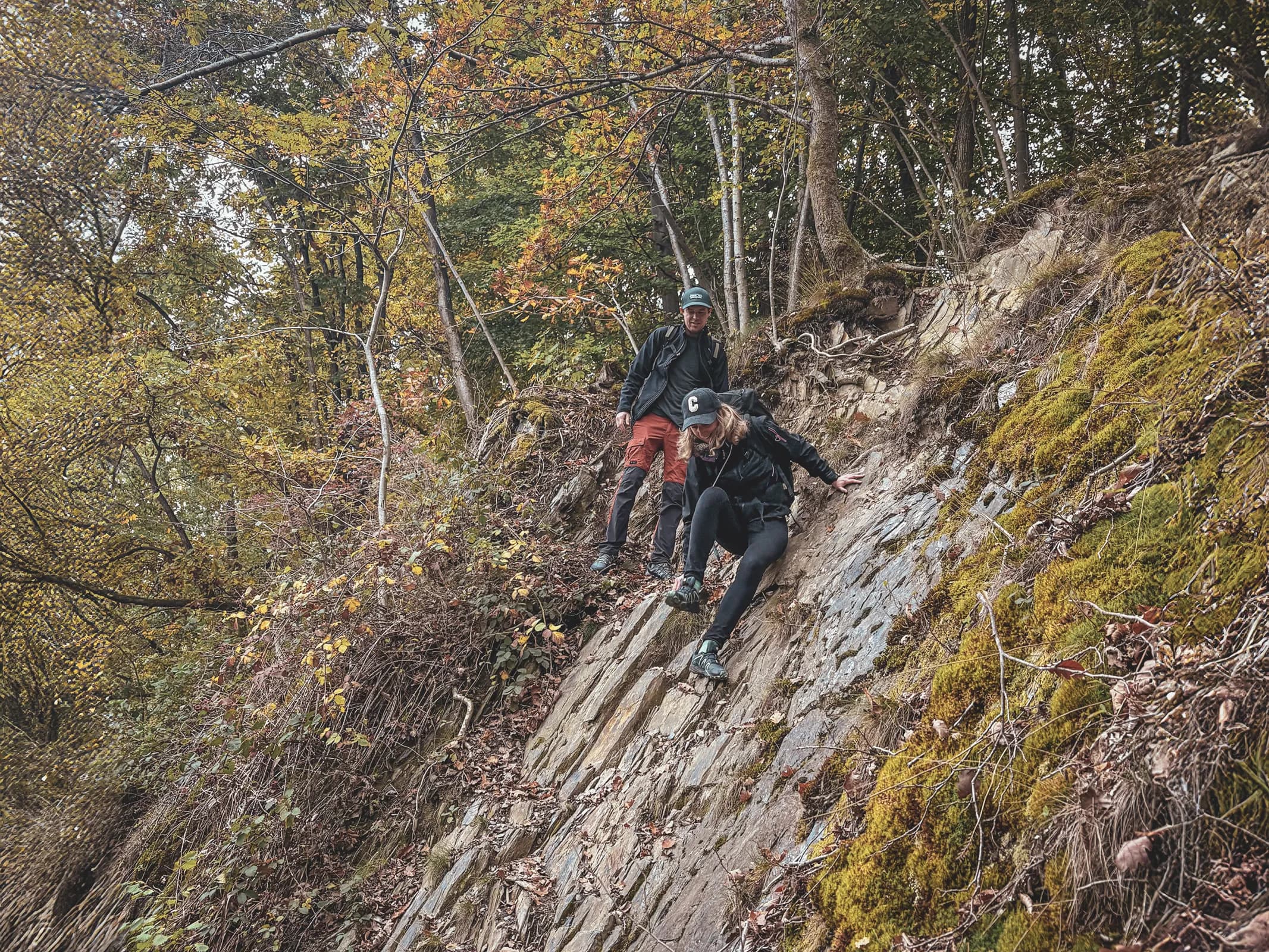 Two hikers descend a steep slope in the middle of the Ardennes forest, surrounded by autumn colours.
