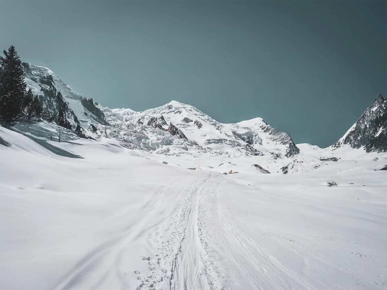 Chemin enneigé menant aux majestueuses montagnes du Mont Blanc sous un ciel clair.