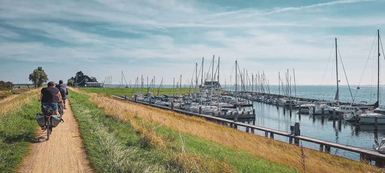 Cyclists on a coastal path, with sailing boats and the sea under a sunny sky.