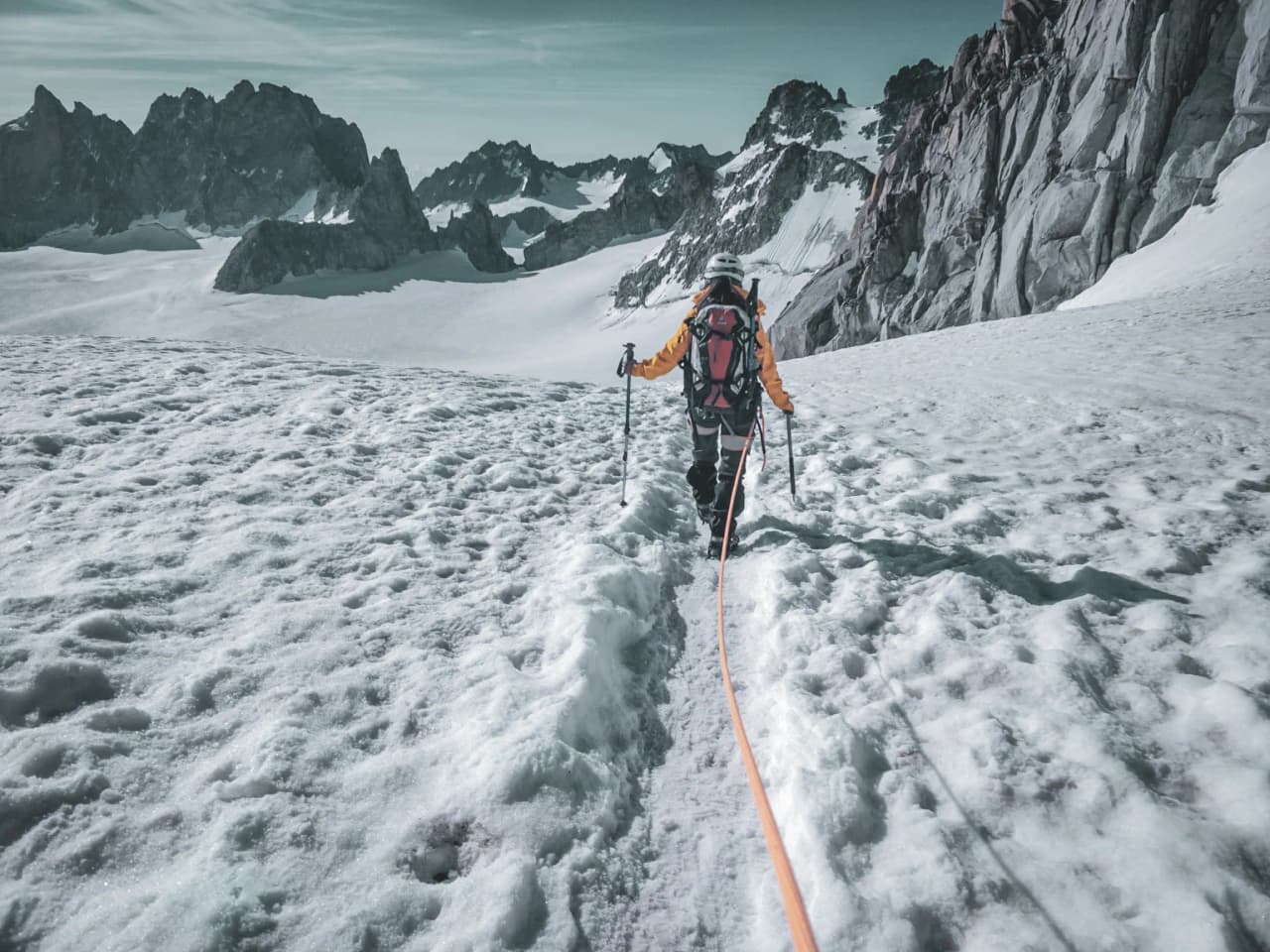 A climber on a glacier, soaring towards the majestic peaks of the Alps, under a clear sky.