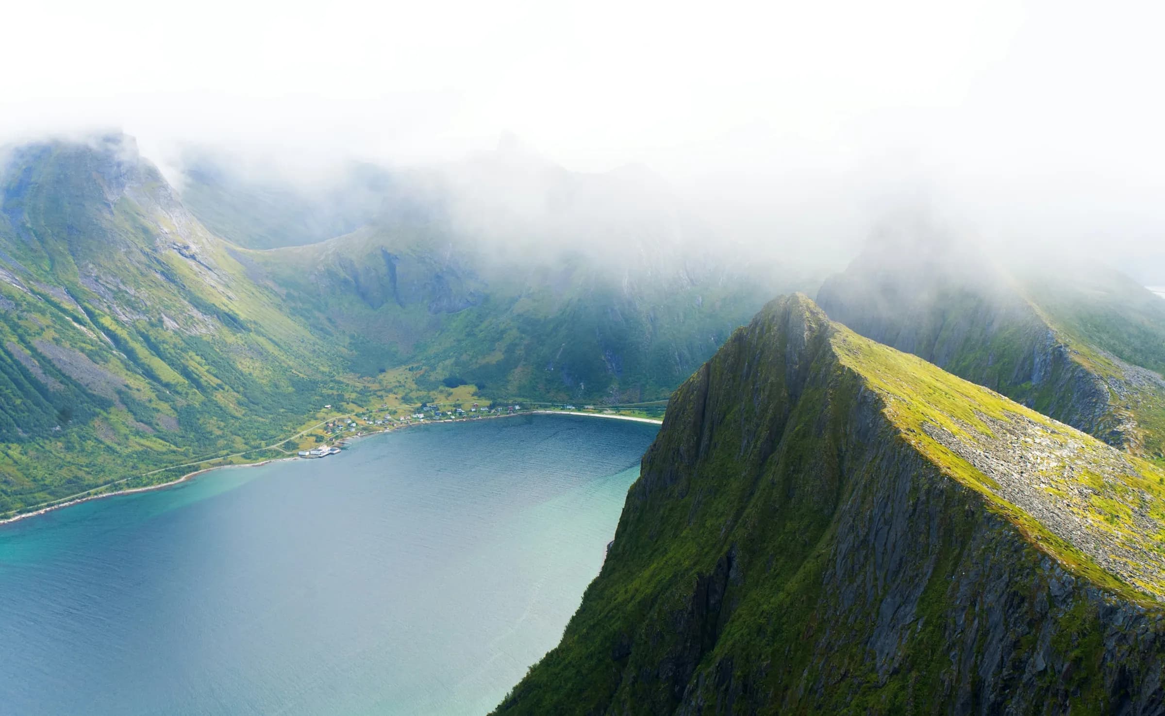 A spectacular landscape on the island of Senja, with fjords, green mountains and a tranquil bay.