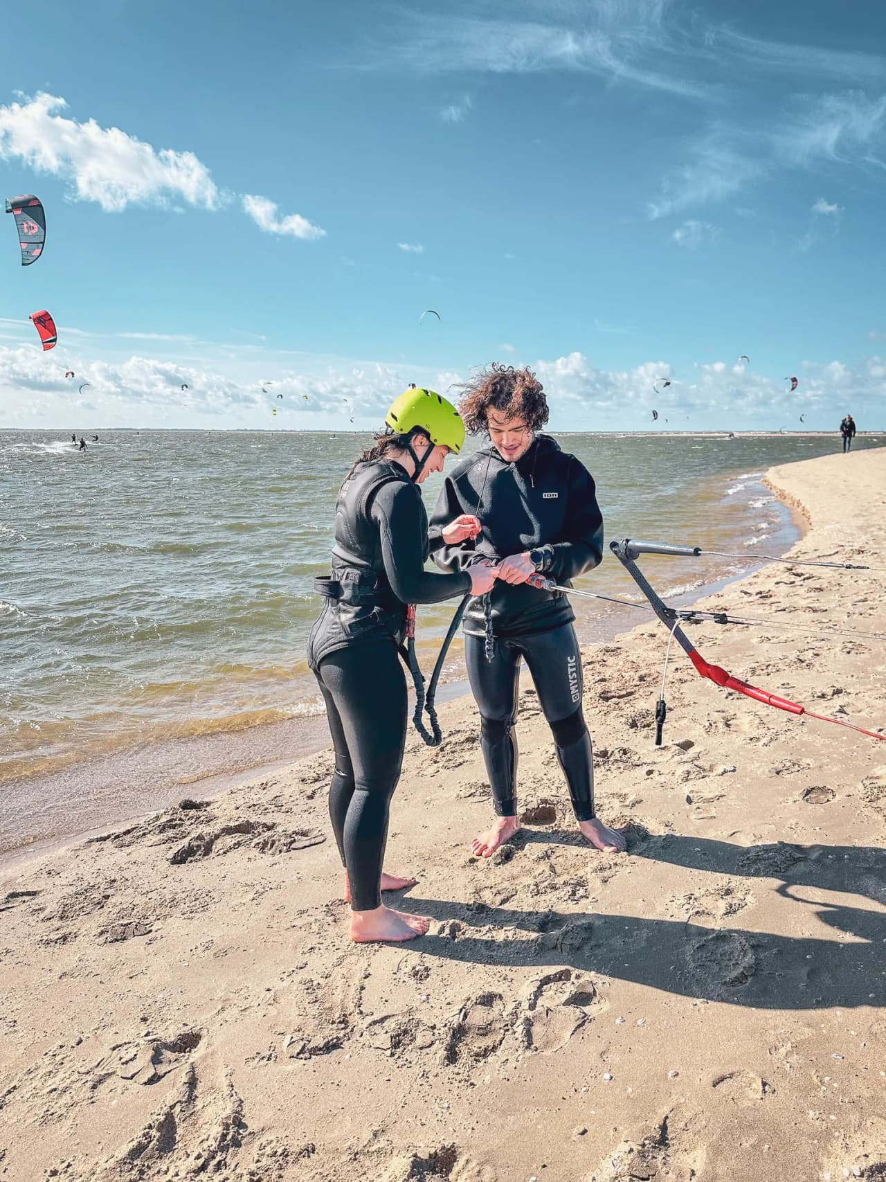 Two people on the beach preparing to kitesurf, under a sunny sky.