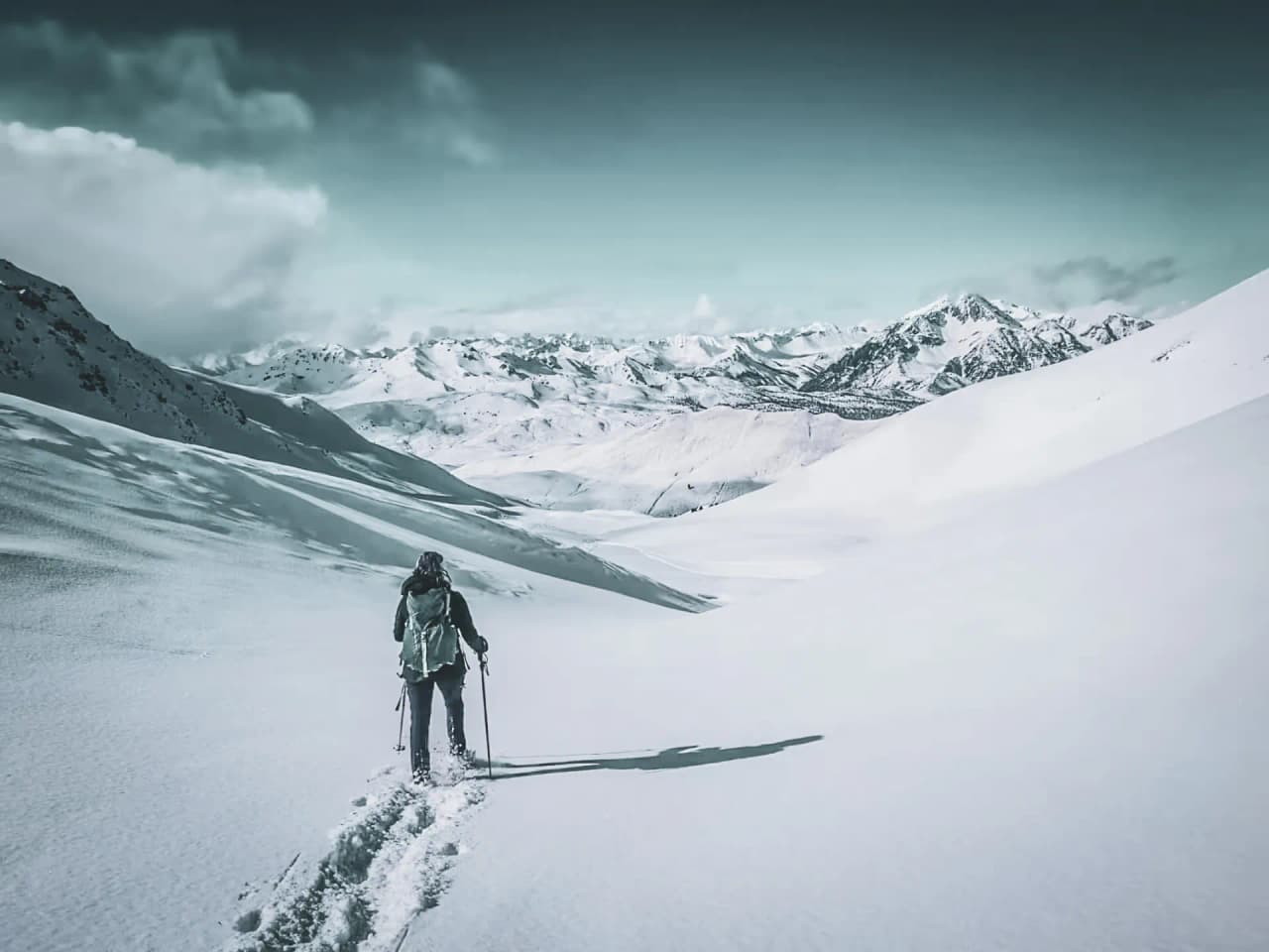 A solitary hiker traversing a snow-covered alpine landscape, past majestic peaks.