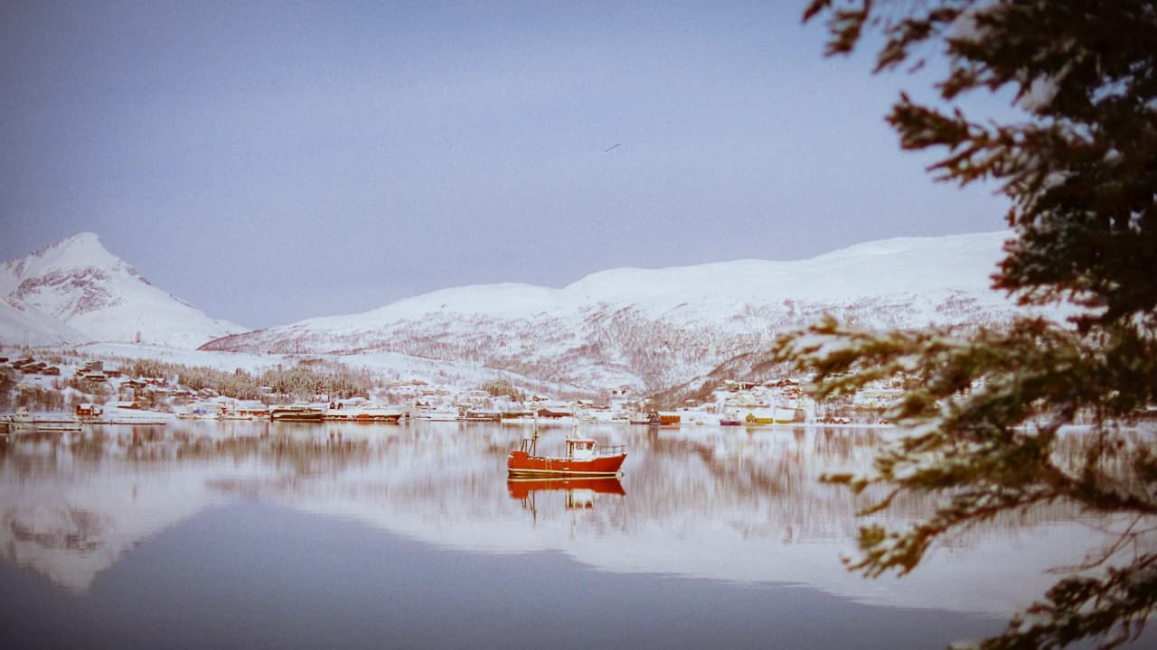 A peaceful Norwegian fjord, with snow-capped mountains and a little red boat.