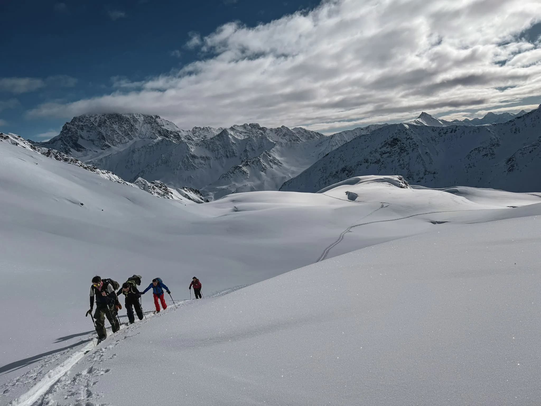 A group of friends ski touring in a majestic snowy landscape, with mountains in the background.