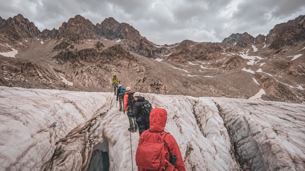 Groupe d'alpinistes traversant un glacier majestueux dans les Écrins, sous un ciel nuageux.