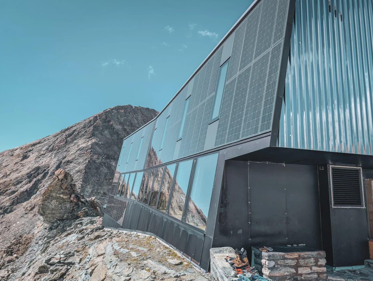 A modern mountain hut, surrounded by majestic rocks under a brilliant blue sky.
