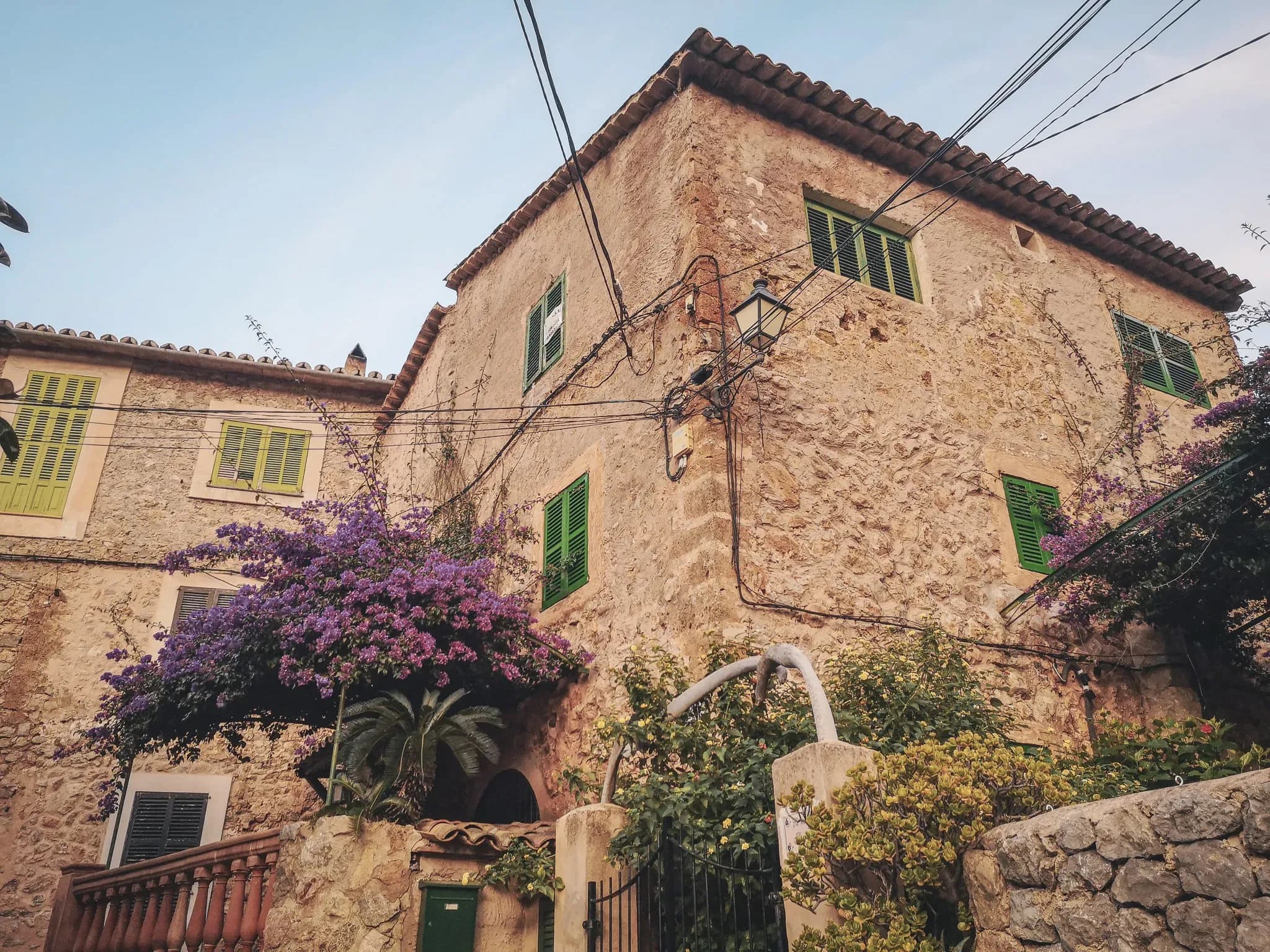 Beautiful stone house with green shutters and purple flowers, typical of Majorca.
