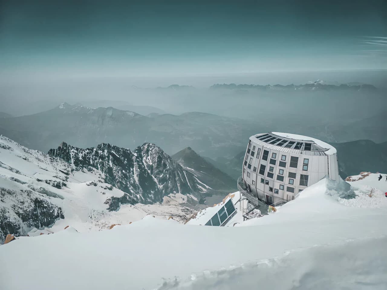 A majestic view of the snow-capped peaks of Mont Blanc and a modern alpine mountain hut under a blue sky.