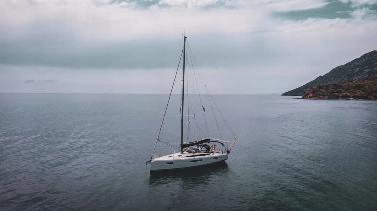 Voilier blanc majestueux dérivant sur les eaux calmes grecques, entouré de paysages idylliques.