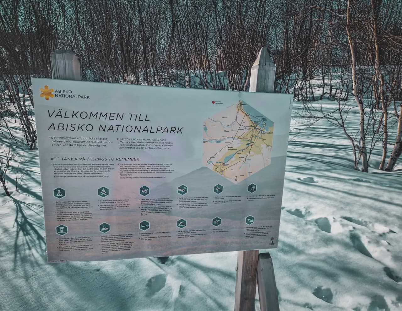 Welkomsbord voor Abisko National Park in Lapland, omgeven door sneeuw en wildernis.