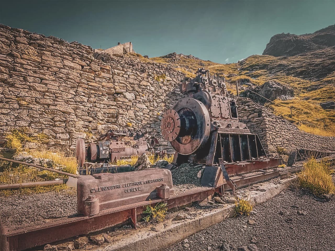 Remains of an old steam engine, surrounded by stone and greenery, evoking adventure.