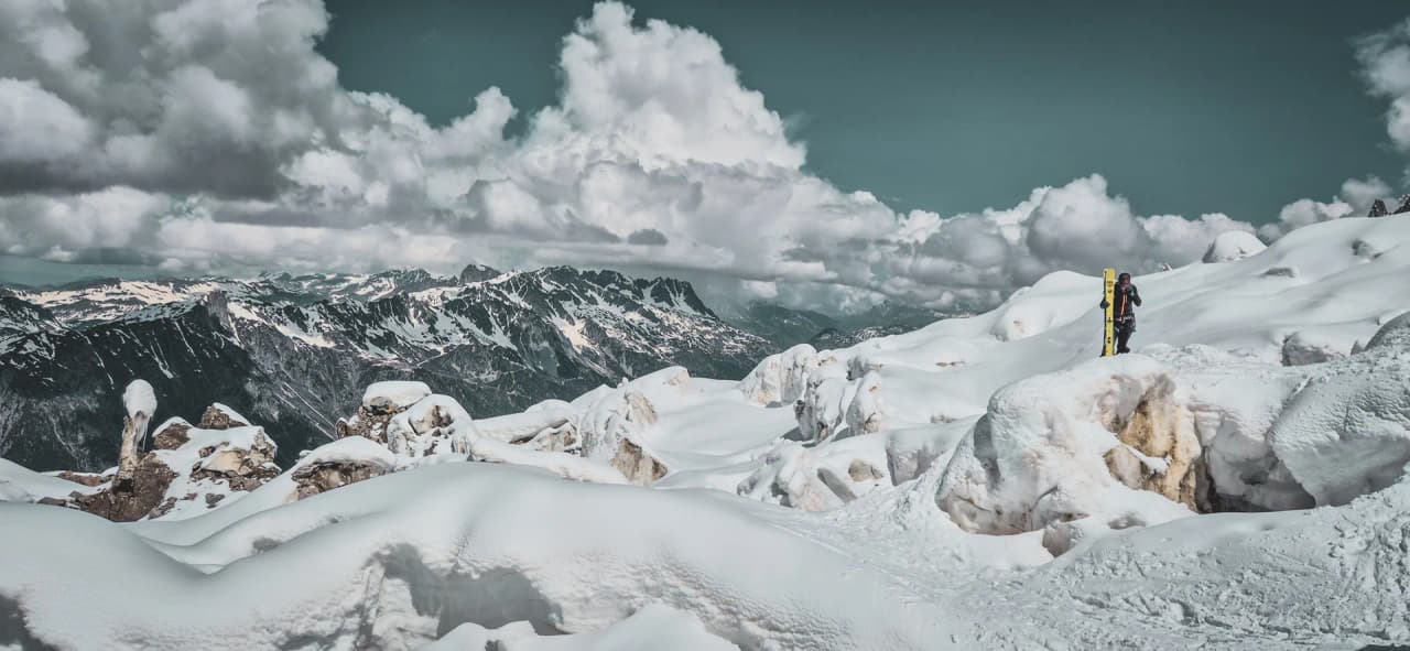 Splendide paysage alpin enneigé, avec un skieur contemplant les sommets majestueux.