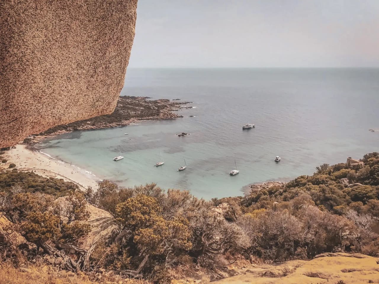 Vue panoramique sur une crique turquoise, avec des voiliers ancrés près d'une plage pittoresque.