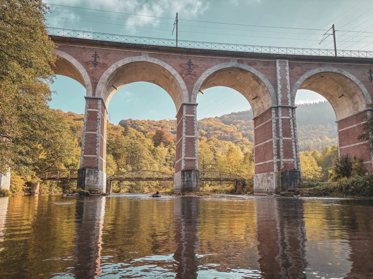In the heart of the Ardennes, a pack racer sails under a majestic viaduct, surrounded by autumn colours.