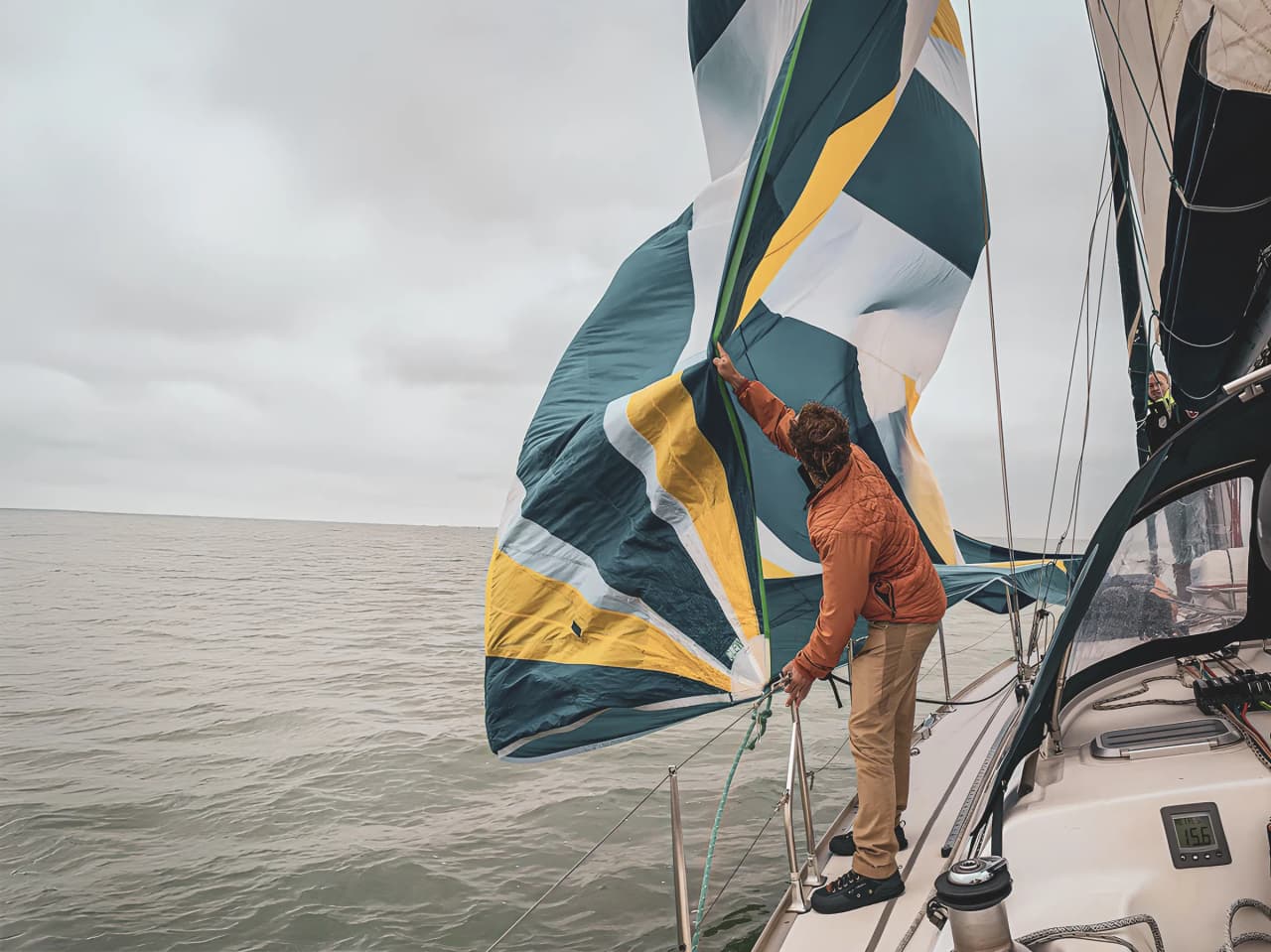 Un marin ajuste une grande voile colorée sur un voilier dans des eaux calmes en pleine aventure.