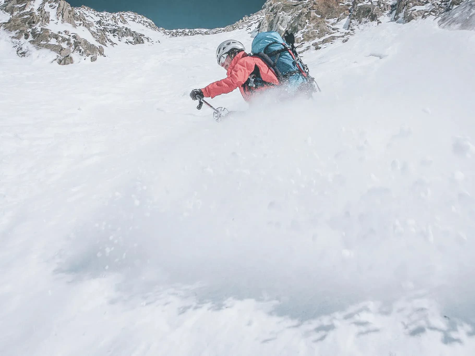 Un skieur dévale une pente glaciaire, éclaboussant des flocons de neige sous un ciel bleu.