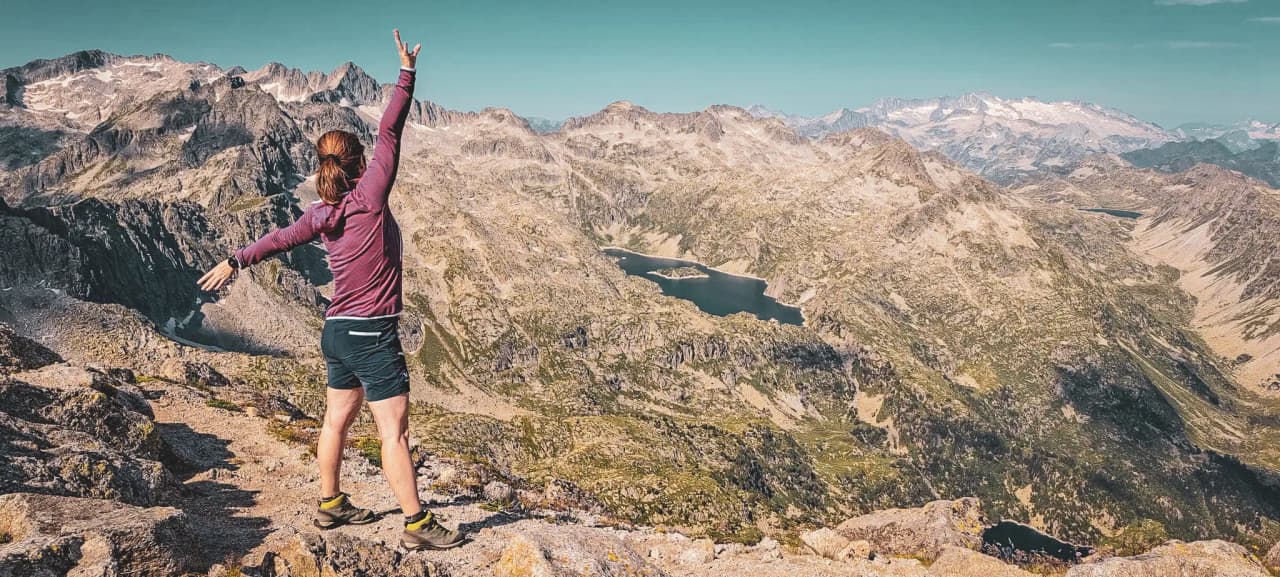 A hiker at the summit admires a splendid panorama of sparkling mountains and lakes.