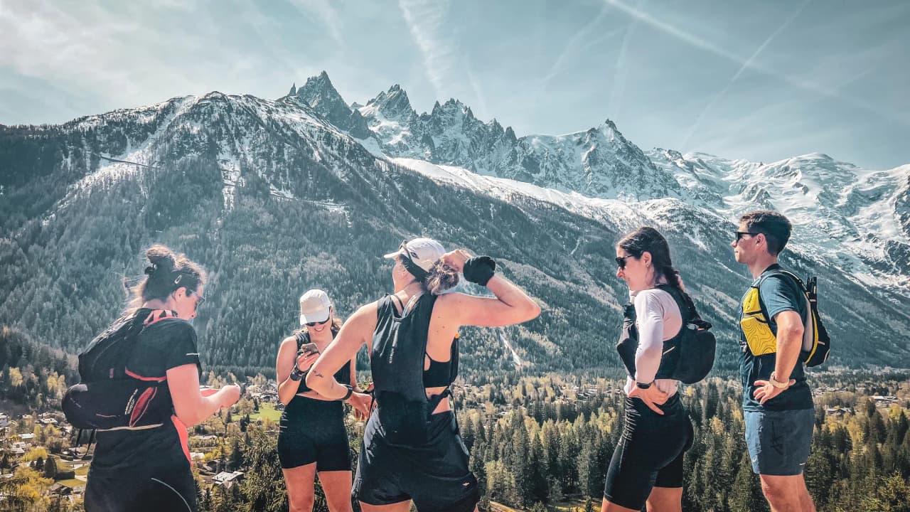 Een groep hardlopers in de bergen, met de besneeuwde toppen van de Mont Blanc op de achtergrond, in een dynamische sfeer.