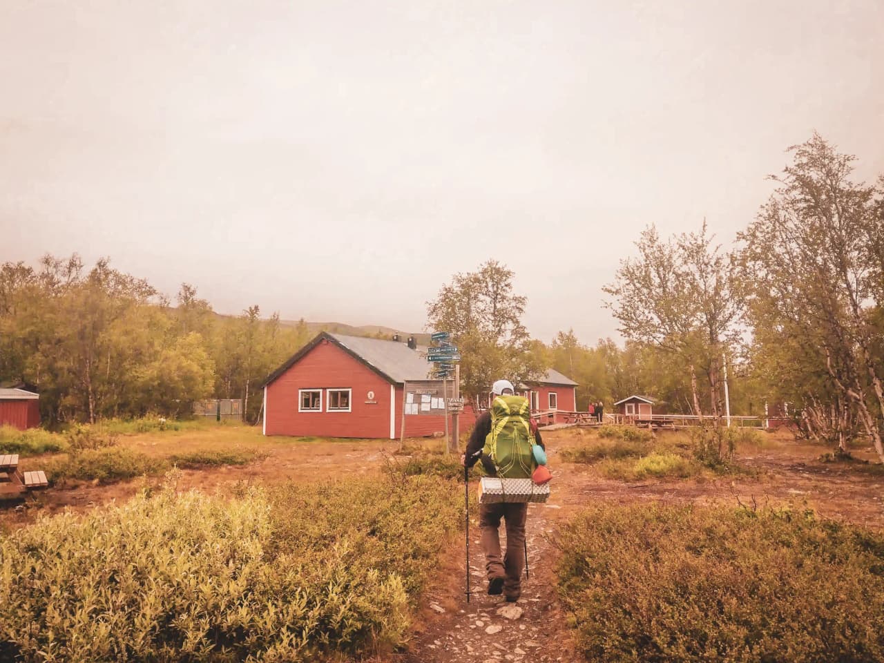 Hiker with a big bag explores the path to picturesque chalets in Swedish Lapland.