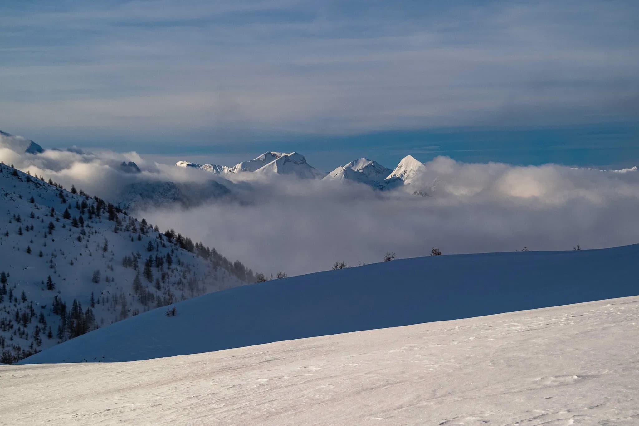 Panorama hivernal des montagnes enneigées, enveloppées de nuages, sur le lac de Serre-Ponçon.