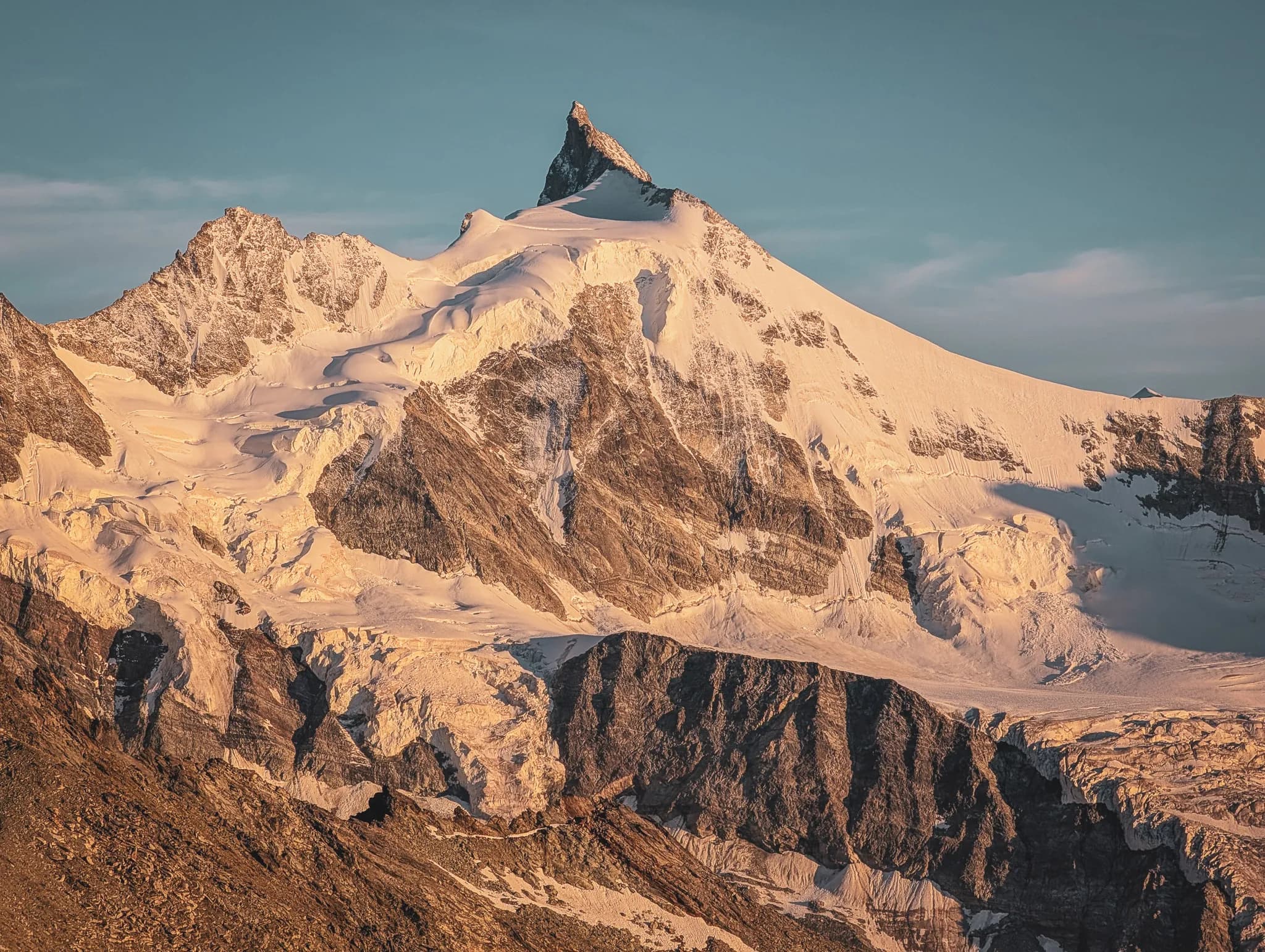 A majestic mountain peak, with craggy crags and eternal snow, stands proudly beneath a blue sky dotted with clouds.