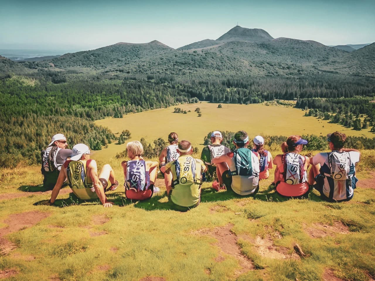 Groupe de randonneurs admirant les volcans d'Auvergne sous un ciel ensoleillé.