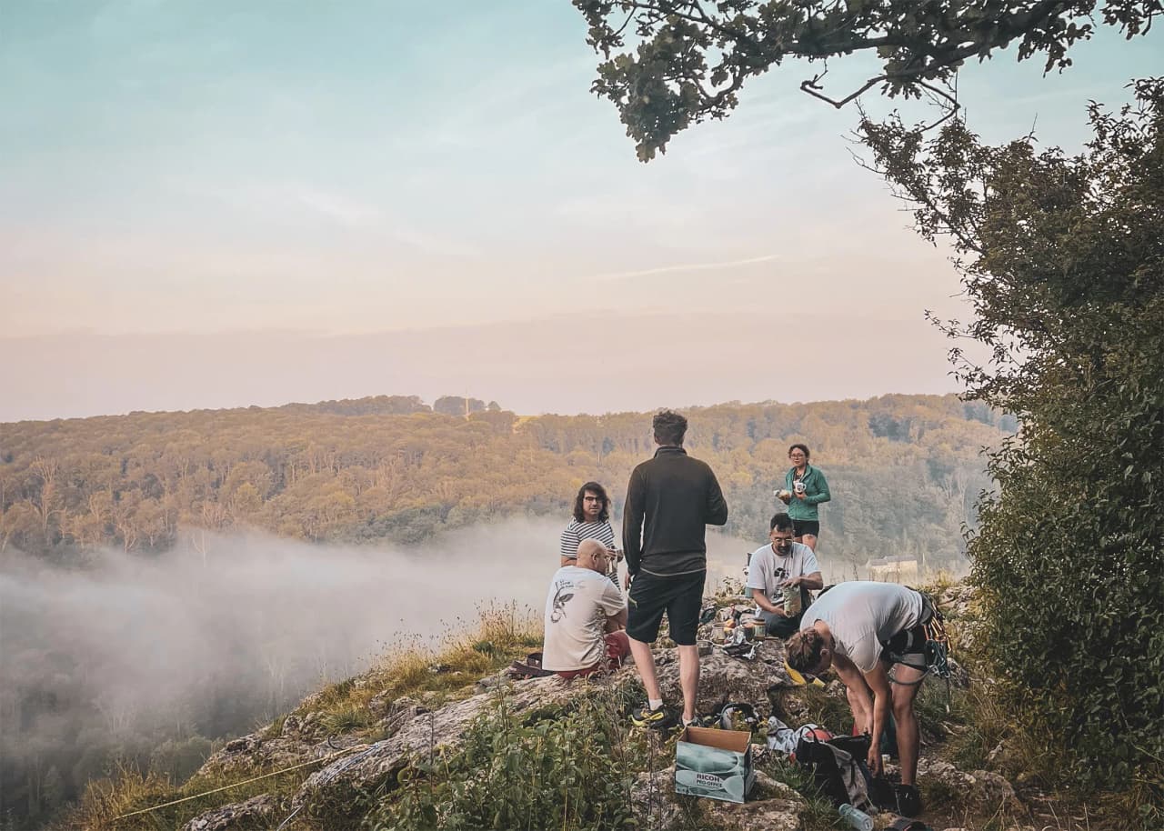 Groupe d'escalade surplombant la vallée brumeuse, ambiance conviviale au crépuscule.