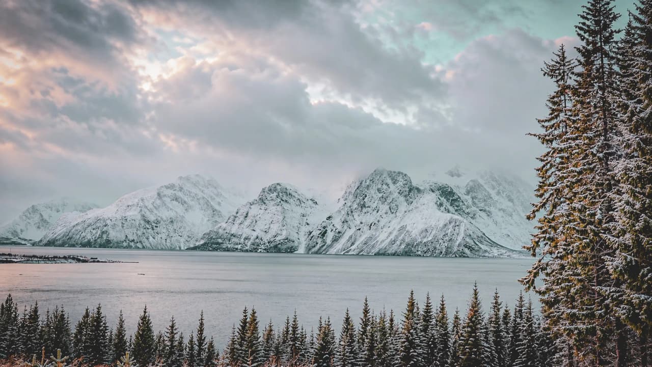 Majestic snow-capped mountains overlooking a peaceful fjord, beneath a cloudy sky.