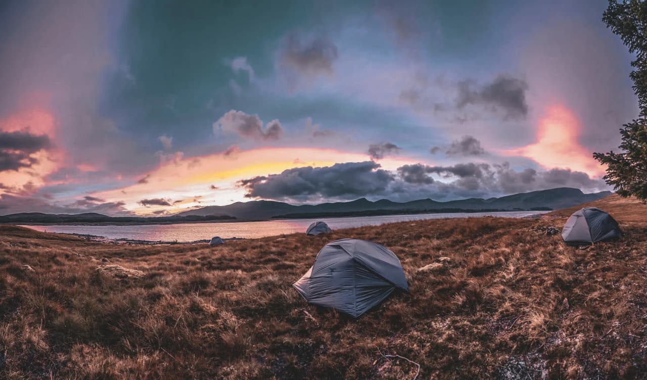 Spectaculaire zonsondergang over de Schotse Hooglanden, tenten bij een vredig loch.