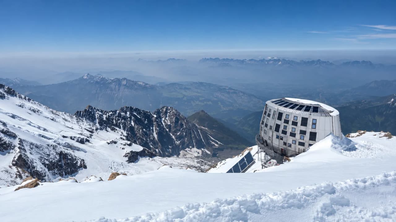 Panorama à couper le souffle des sommets enneigés, avec un refuge moderne entre ciel et montagne.