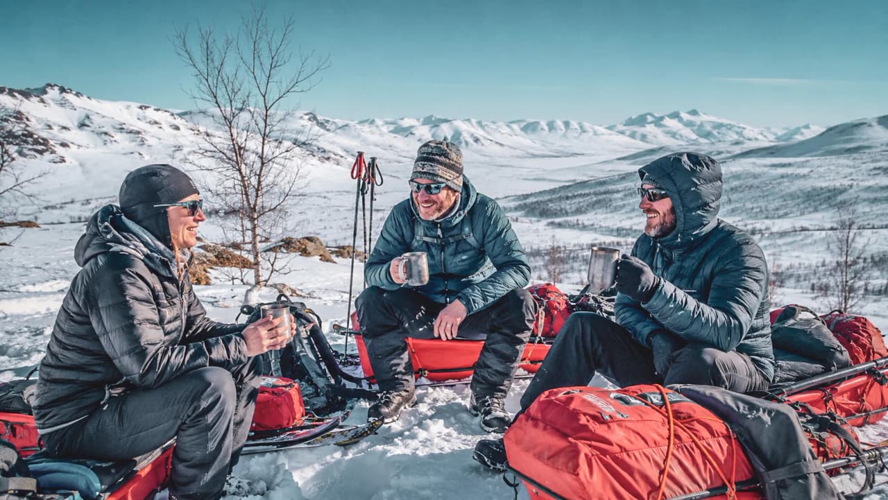 Drie glimlachende avonturiers nemen een koffiepauze in een besneeuwd landschap in Noors Lapland.