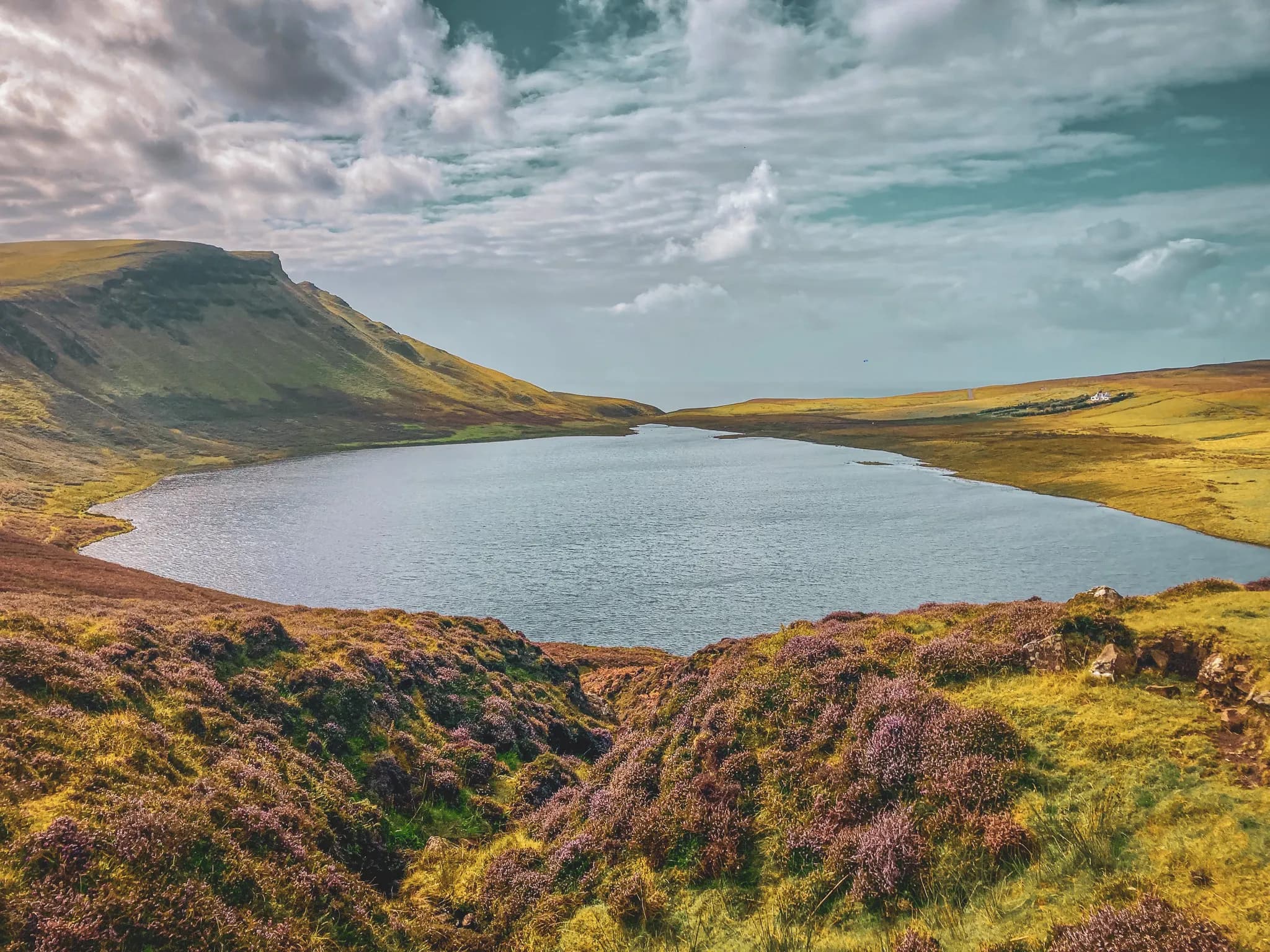 A peaceful lake surrounded by green hills and purple heather on the Isle of Skye.