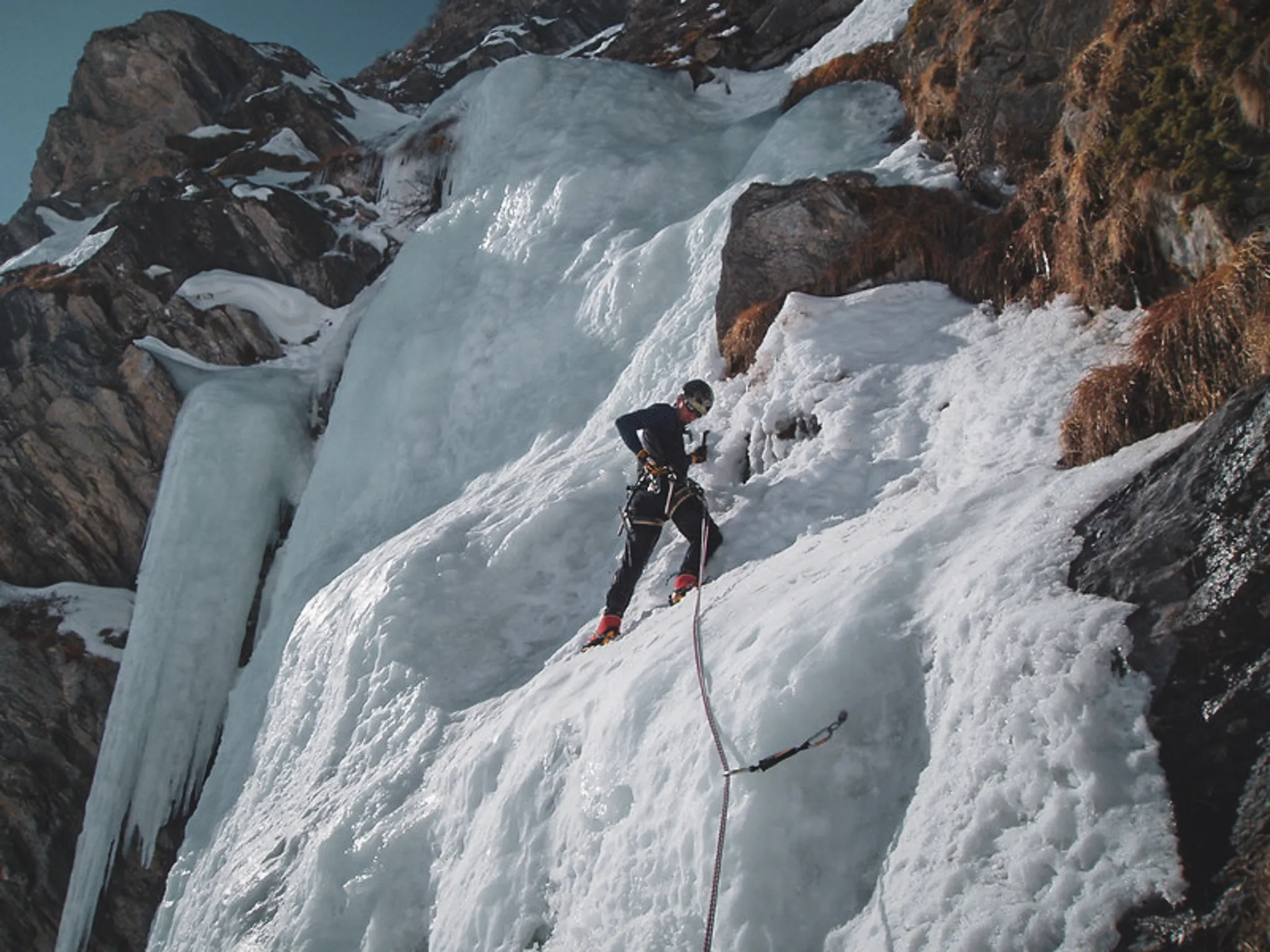 Een klimmer in volle beklimming van een ijsval in de zonnige Italiaanse Alpen.