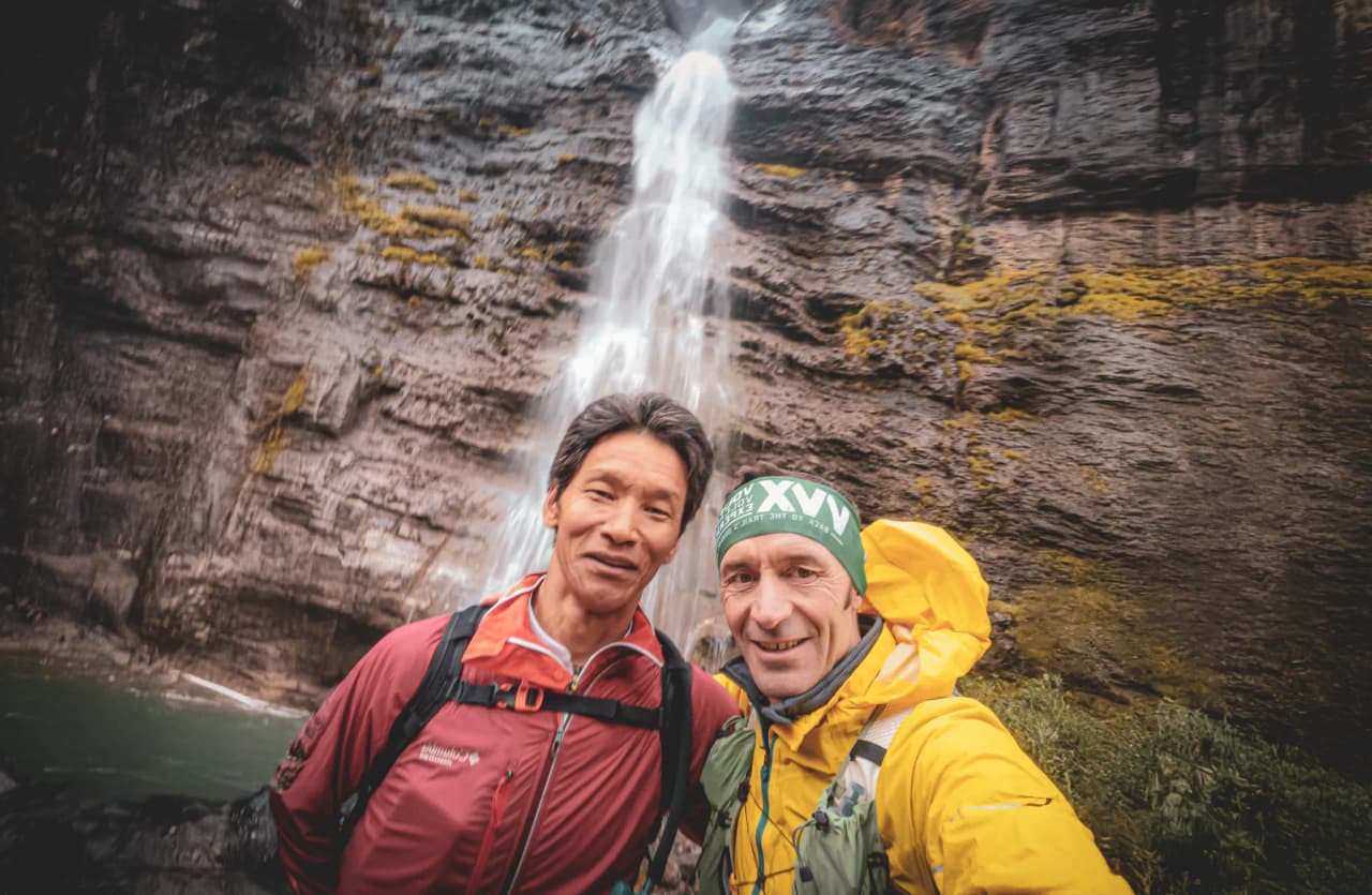 Deux randonneurs souriants devant une cascade majestueuse dans le Parc national du Mercantour.