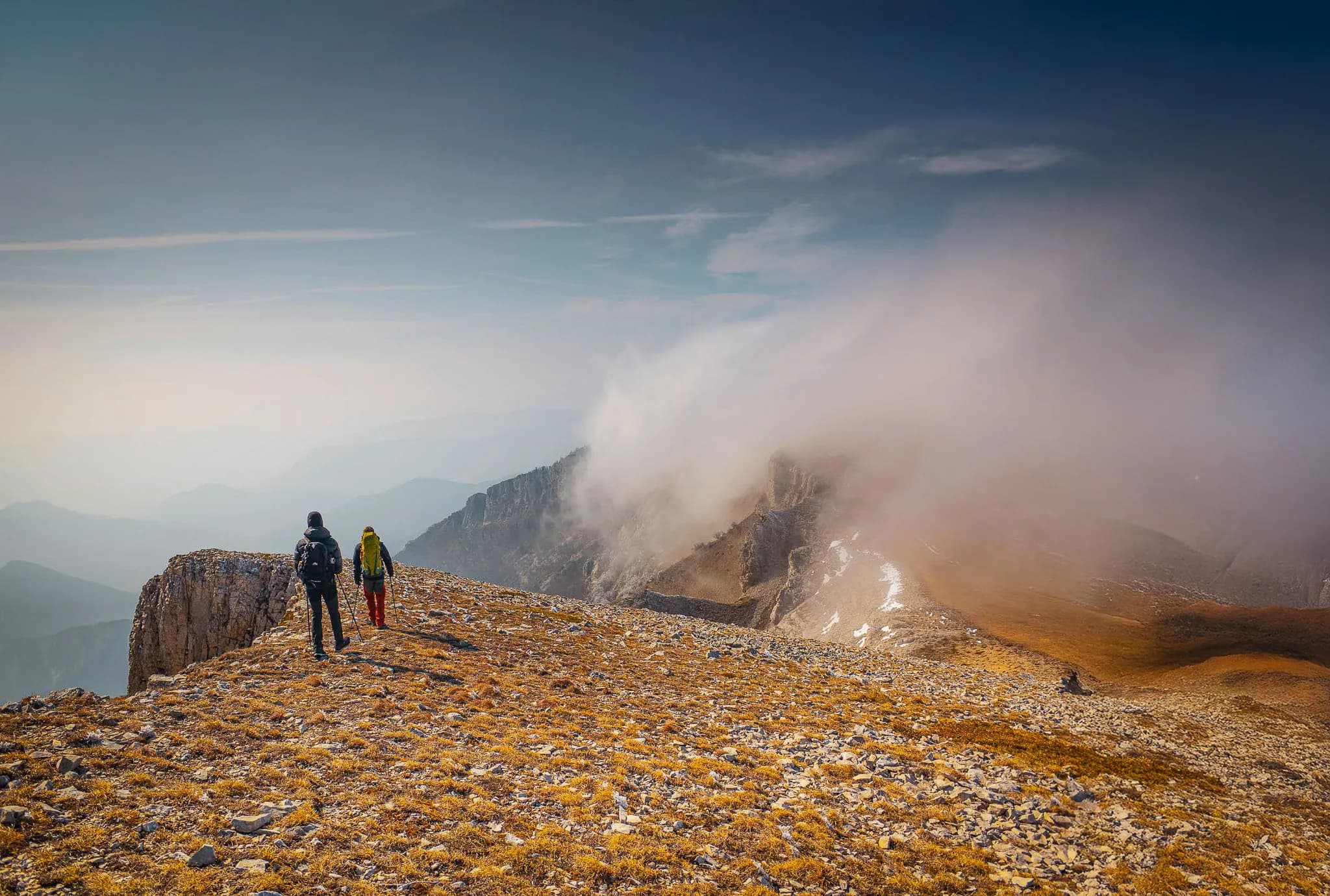Two hikers explore a striking mountain landscape under a cloudy Vercors sky.