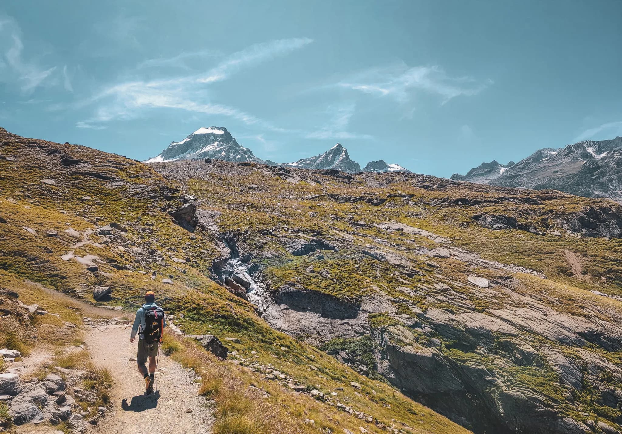 A climber on a green path with the snow-capped peaks of Gran Paradiso in the background.