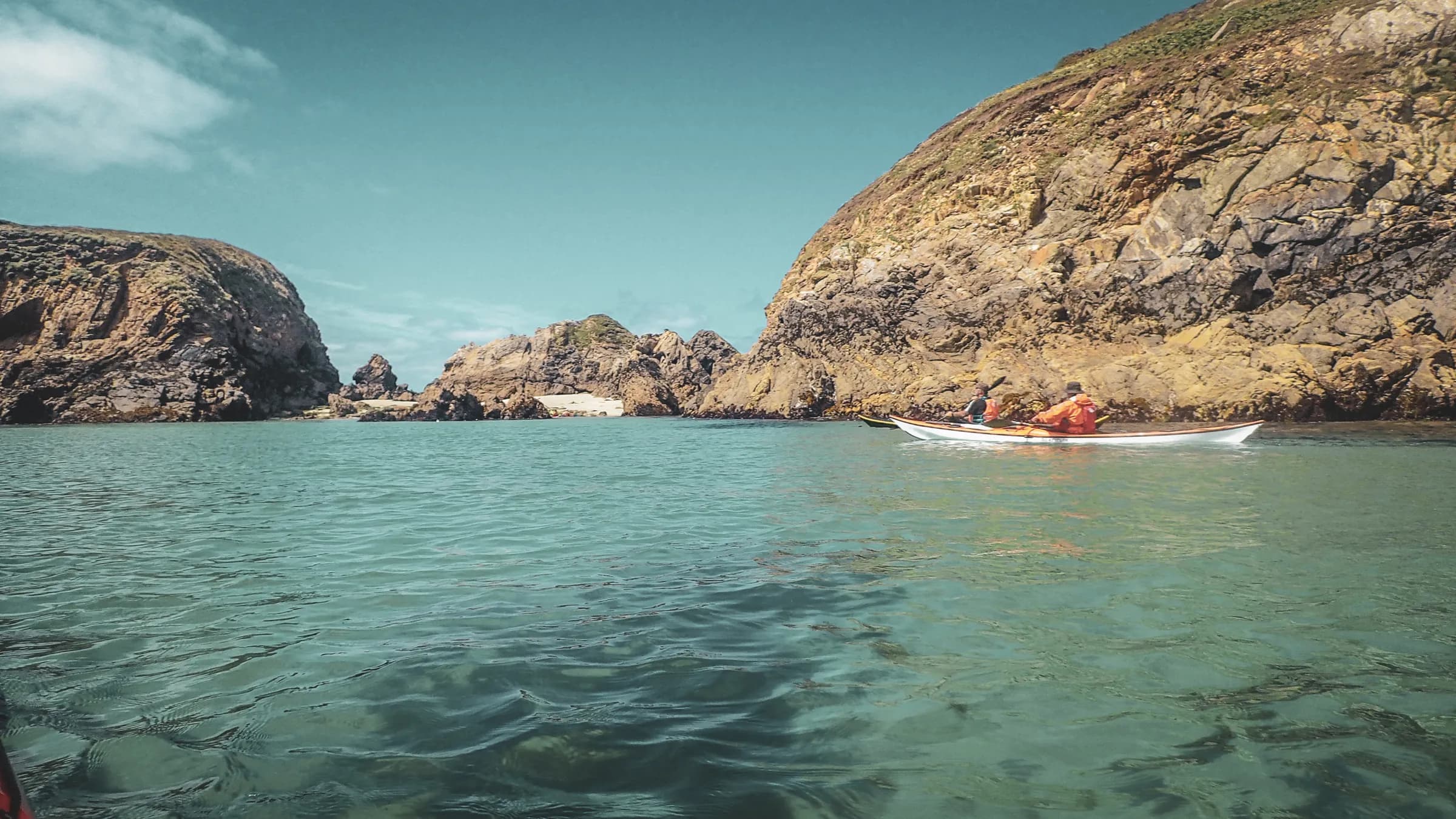 A kayak glides over crystal-clear waters between sun-drenched rocky islands.