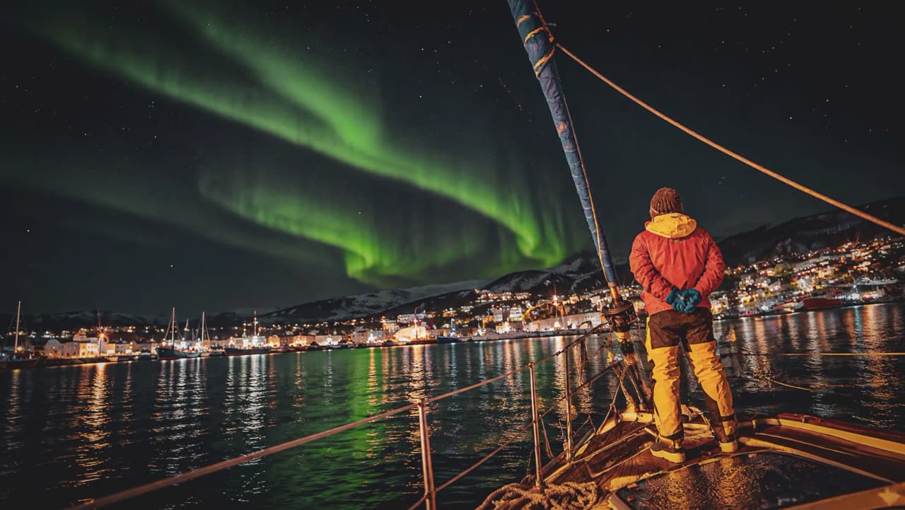 A sailing boat in the moonlight beneath the Northern Lights in Tromsø, offering a magical adventure.